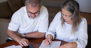 Before taking tax-free pension cash, consider the problems it can create later: an older couple going through pension and retirement paperwork together at home