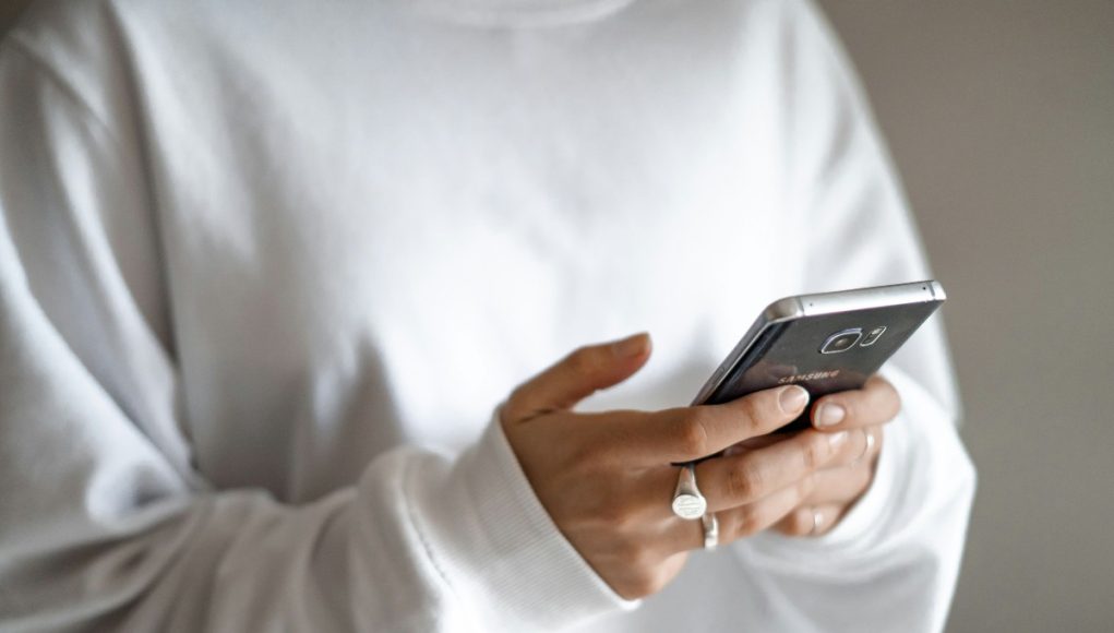 Budget limits, waiting periods and planned repayments can curb stress-driven spending: a person in a white jumper checking their household budget on a mobile phone
