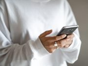 Budget limits, waiting periods and planned repayments can curb stress-driven spending: a person in a white jumper checking their household budget on a mobile phone
