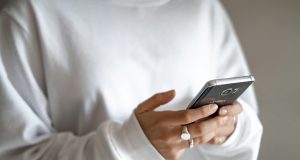 Budget limits, waiting periods and planned repayments can curb stress-driven spending: a person in a white jumper checking their household budget on a mobile phone